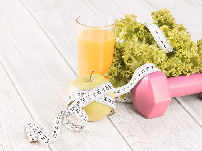 Gesunde Ernährung Ein Glas Orangensaft, ein Apfel, Salat und ein rosa Gewicht liegen auf einem Tisch und sind mit einem Maßband umwickelt