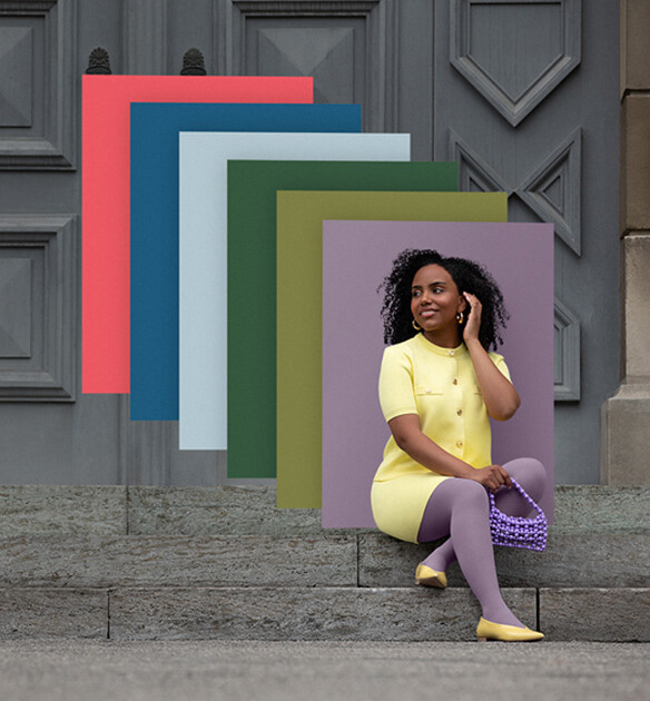 Eine Frau sitzt auf Steinstufen vor einem Tor. Sie trägt einen hellgelben Zweiteiler zu einer lilanen Kompressionsversorgung. Hinter ihr sieht man Farbfelder in den Trend Colours