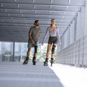Um homem e uma mulher, ambos com uma joelheira, andam de patins numa garagem