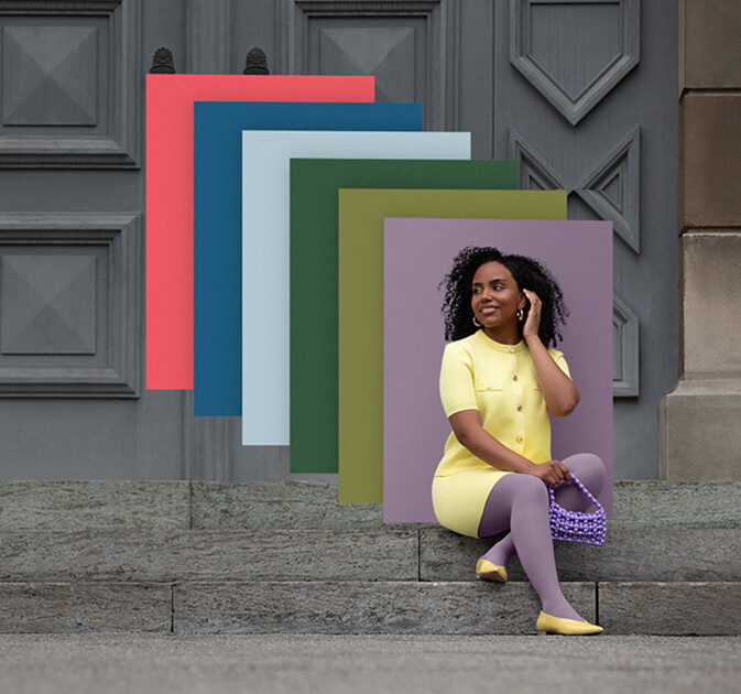 Una donna siede di fronte a un muro fiorito. Indossa un trattamento compressivo in colore giallo con motivo Batik bianco