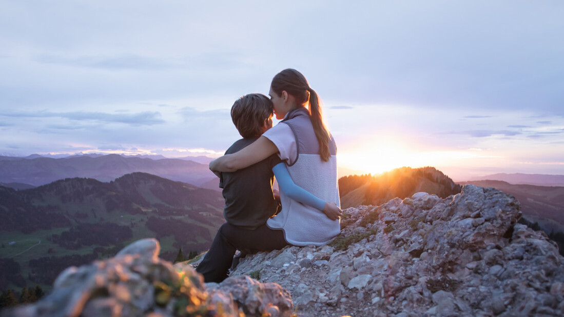 Une mère est assise avec son enfant au sommet d'une montagne. L'enfant porte une manchette de compression. Une mère est assise avec son enfant au sommet d'une montagne. L'enfant porte une manchette de compression.