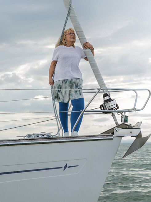Una donna affetta da linfedema è in piedi sul ponte di una barca. Indossa calze compressive blu.