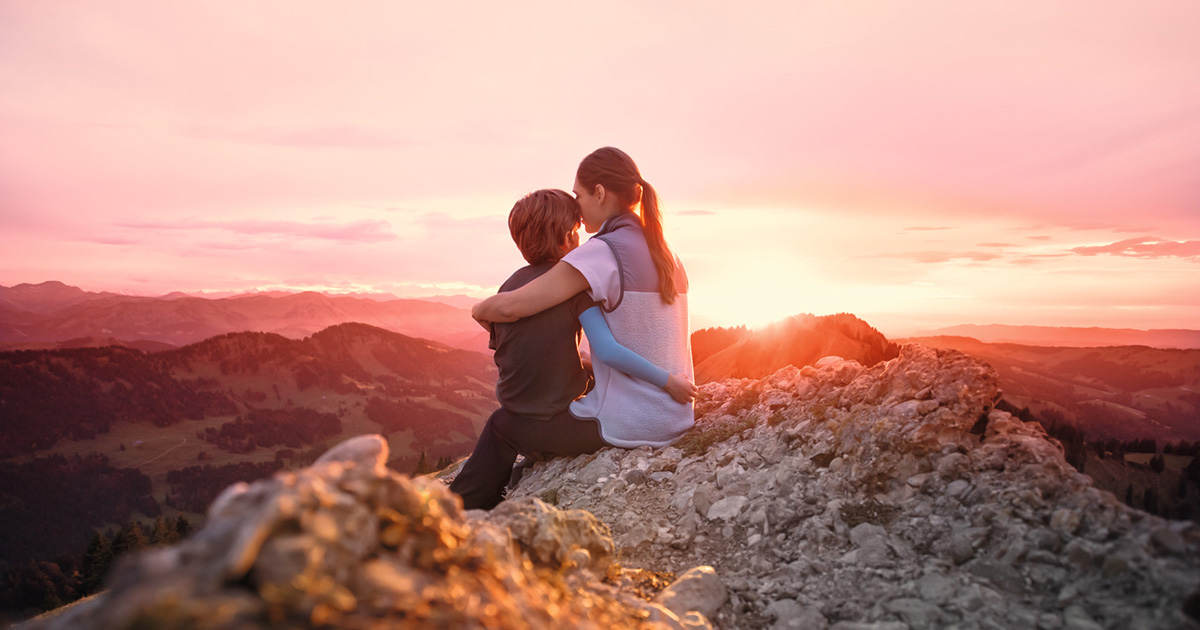 Une mère est assise avec son enfant au sommet d'une montagne. L'enfant porte une manchette de compression.